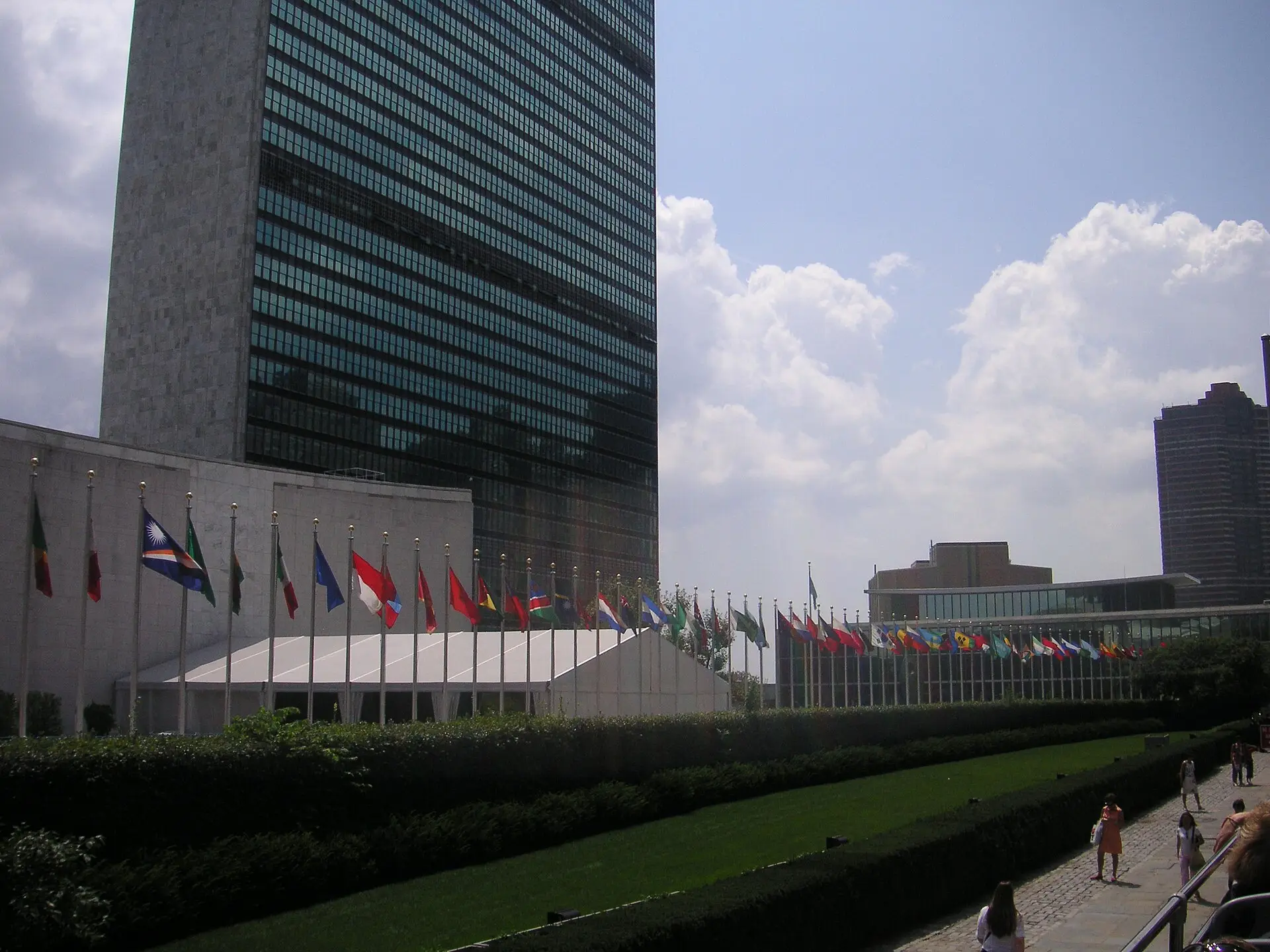 The United Nations Secretariat tower in New York with a long row of member states' flags along the lawn.