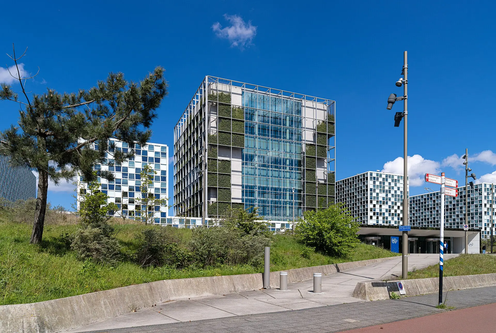 The International Criminal Court building in The Hague, a glass tower wrapped in greenery, under a blue sky.