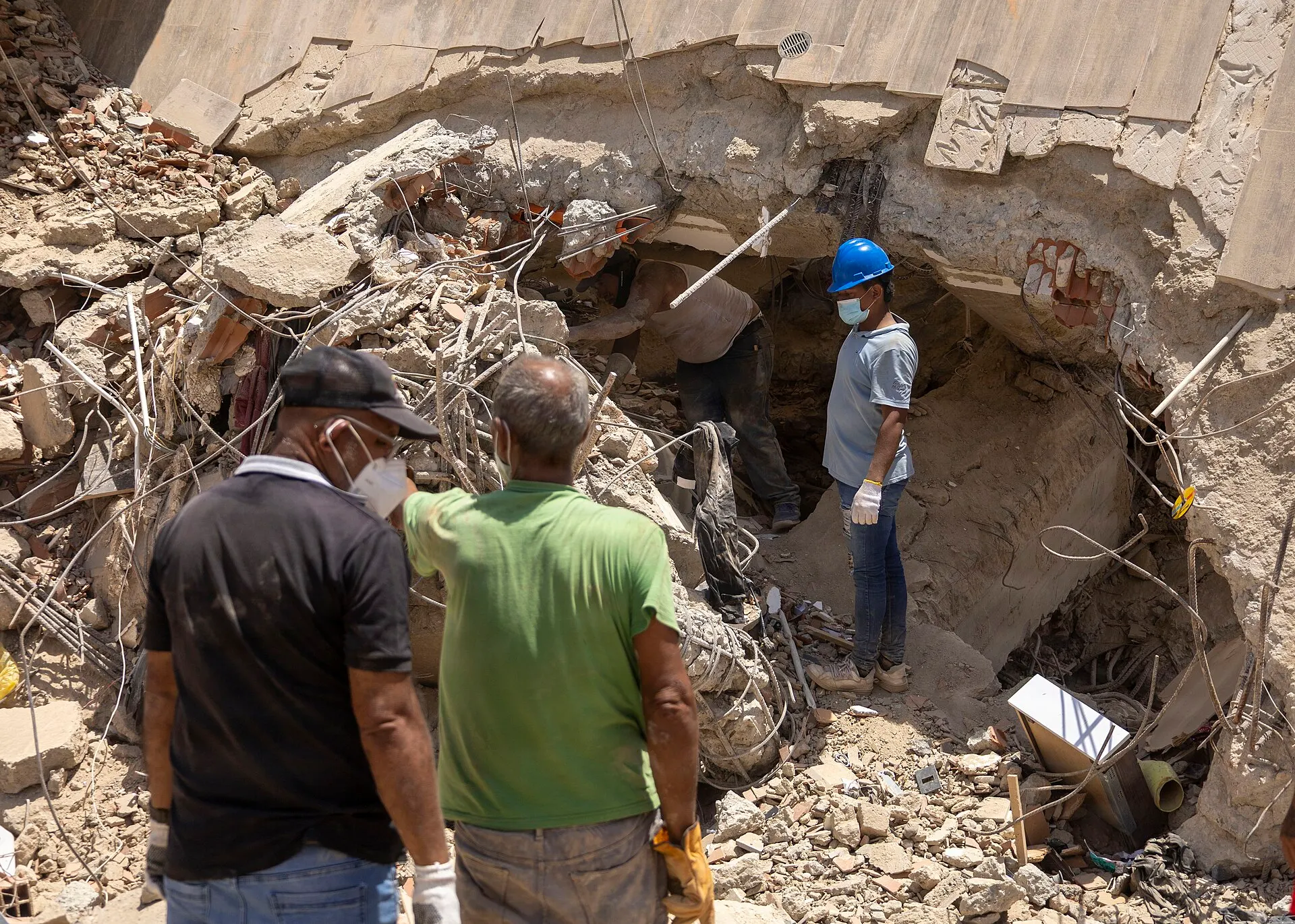 Men in masks and gloves search through the rubble of a collapsed building in La Guaira, Venezuela.