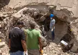 Hombres con mascarillas y guantes buscan entre los escombros de un edificio derrumbado en La Guaira, Venezuela.