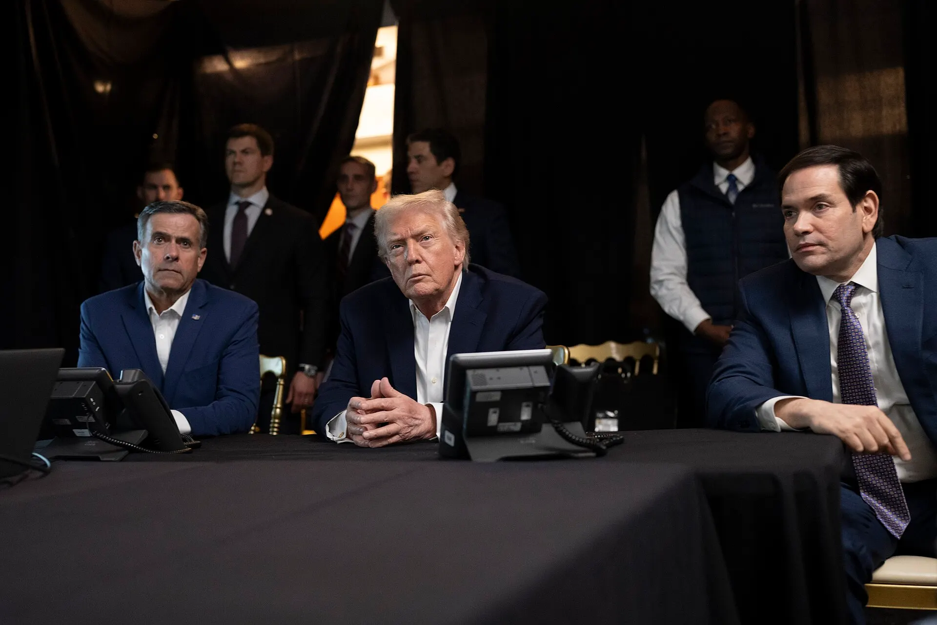 Donald Trump sits between John Ratcliffe and Marco Rubio at a table with monitors at Mar-a-Lago.