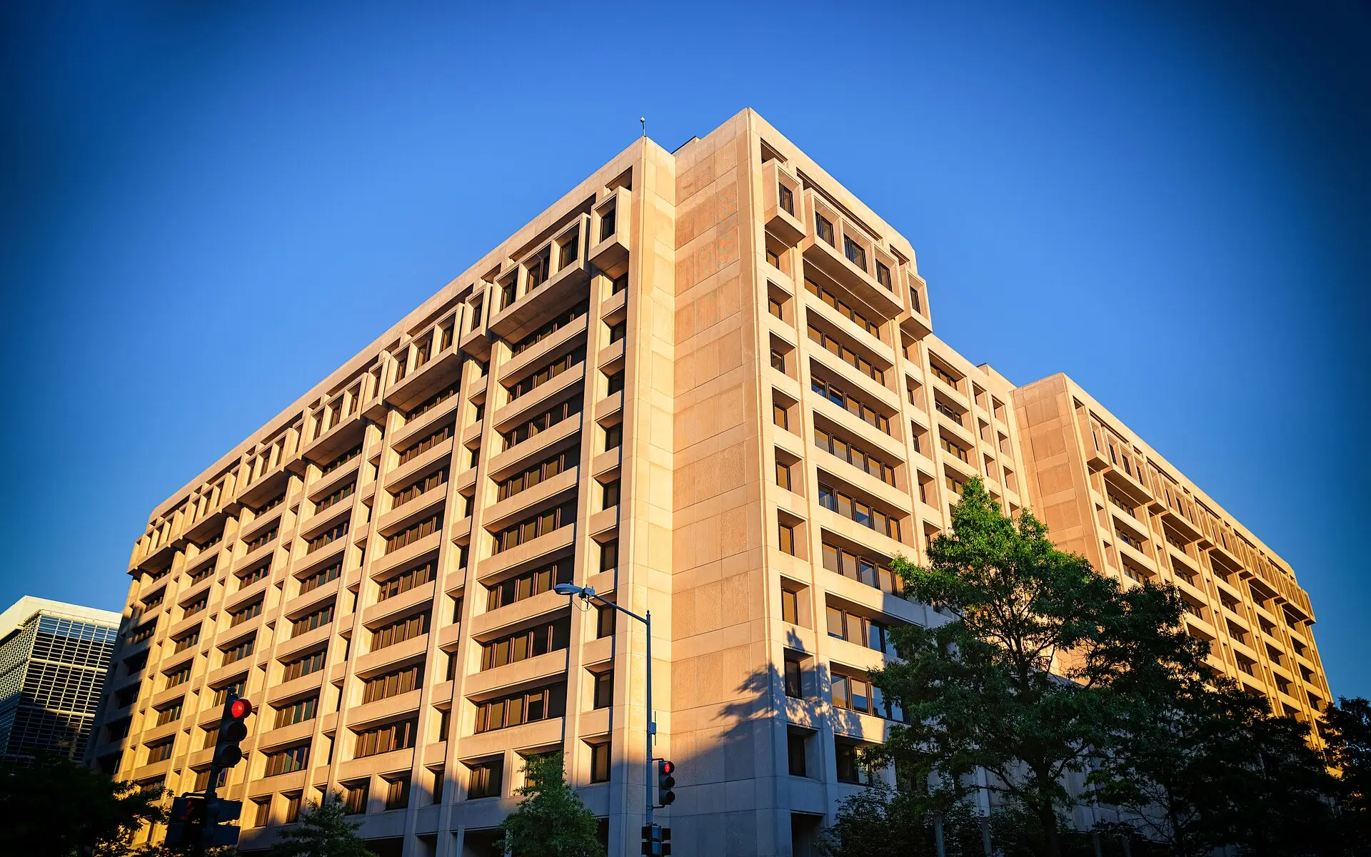 The tall beige International Monetary Fund headquarters building in Washington, D.C., against a clear blue sky.