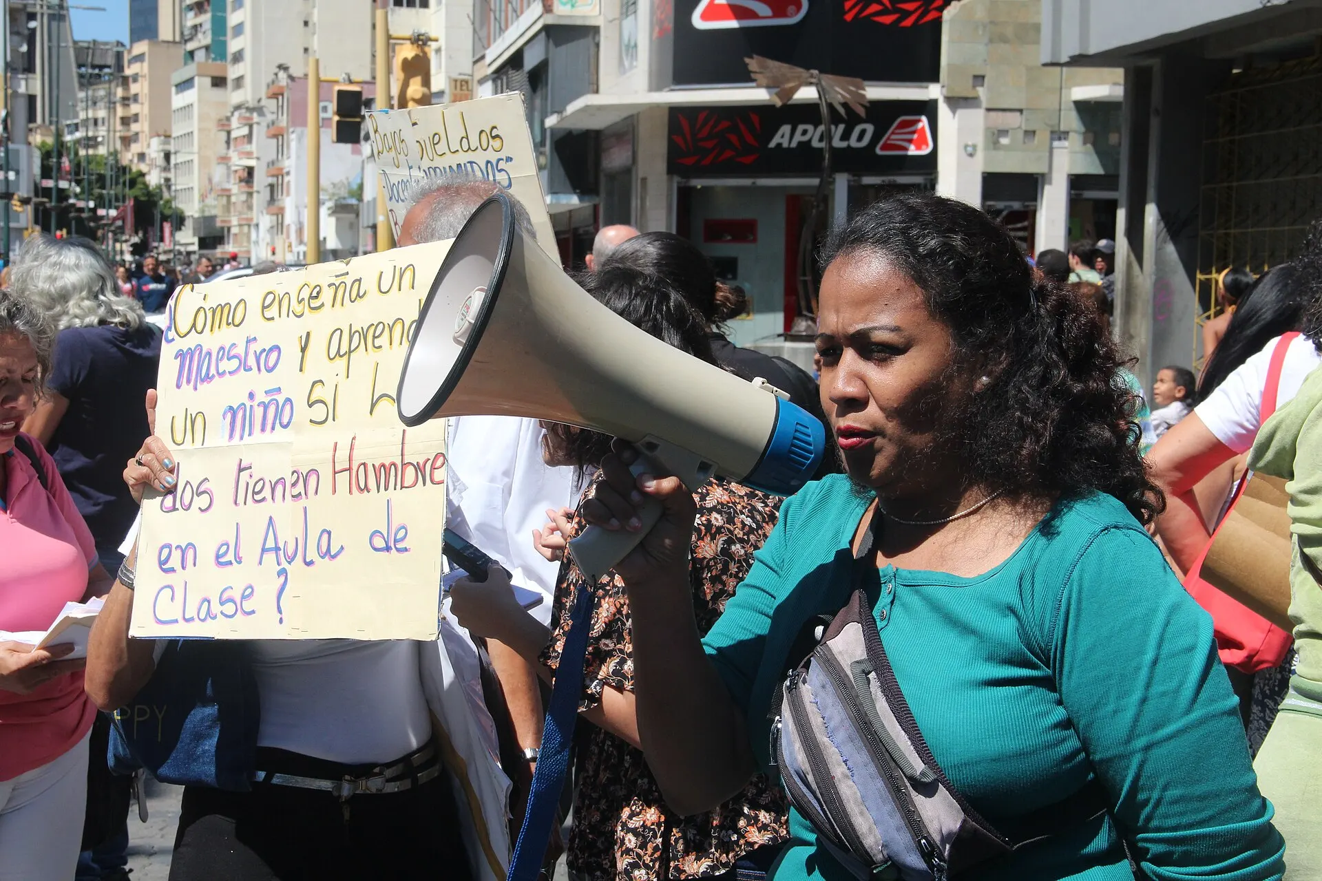 A teacher with a megaphone protests in Caracas beside a sign asking how teachers and children can work while hungry.
