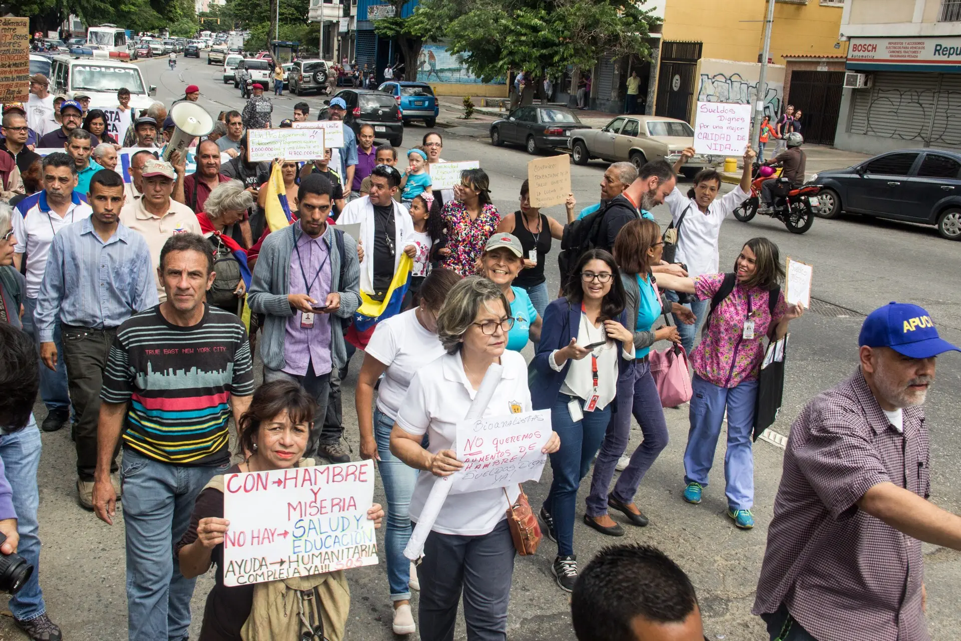 Workers and older Venezuelans march down a Caracas street with handmade signs demanding decent wages.