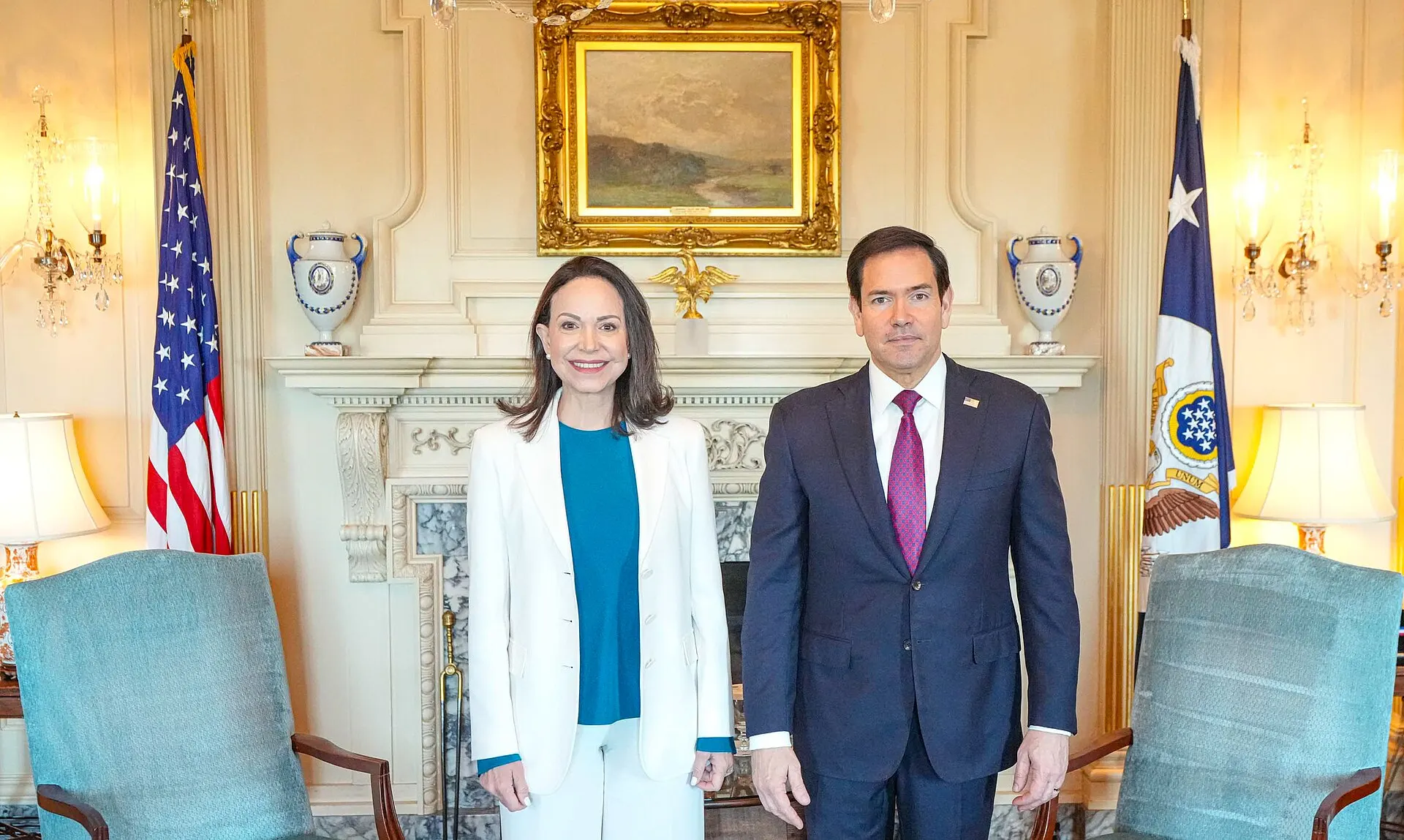 María Corina Machado, in a white jacket, stands beside U.S. Secretary of State Marco Rubio in a formal reception room.