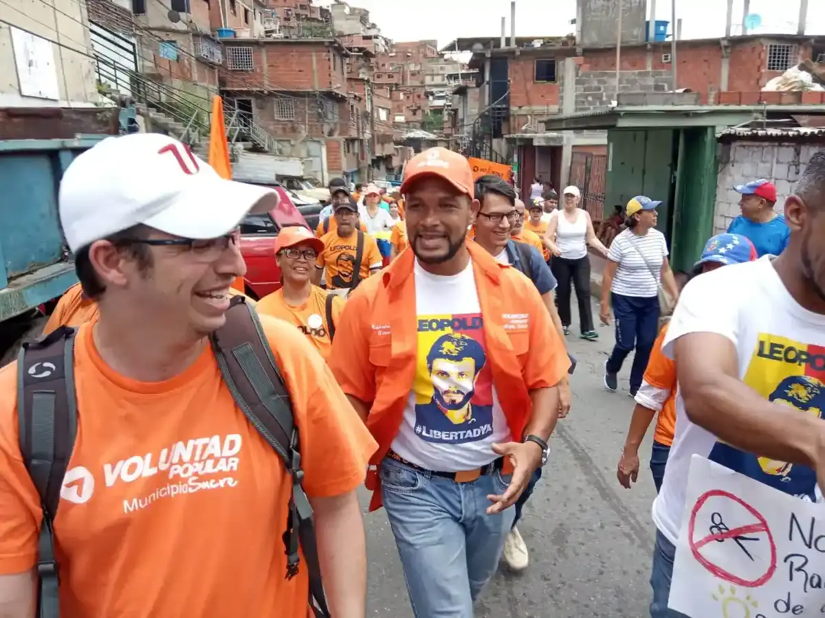 Voluntad Popular activists in orange walk through a hillside neighborhood.