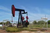 A red and blue oil pumpjack inside a wire fence in an oil field in Zulia, Venezuela, under a blue sky.