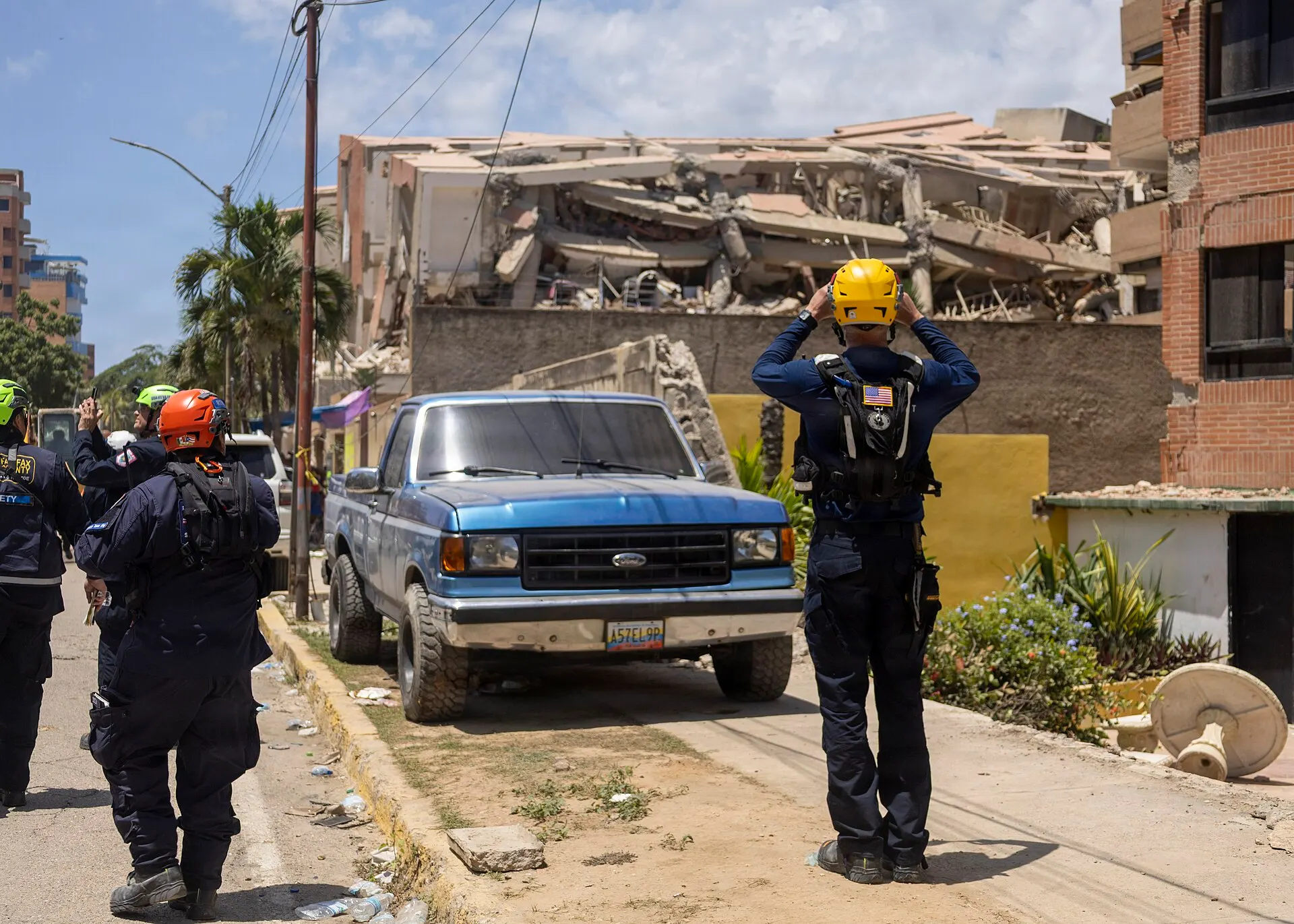 Rescue workers in helmets stand in a street before a collapsed multi-storey building in La Guaira, Venezuela.