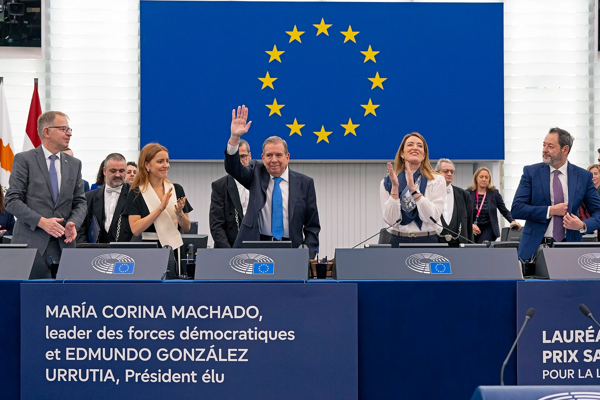 Edmundo González Urrutia waves in the European Parliament as MEPs applaud; a banner names him and María Corina Machado.