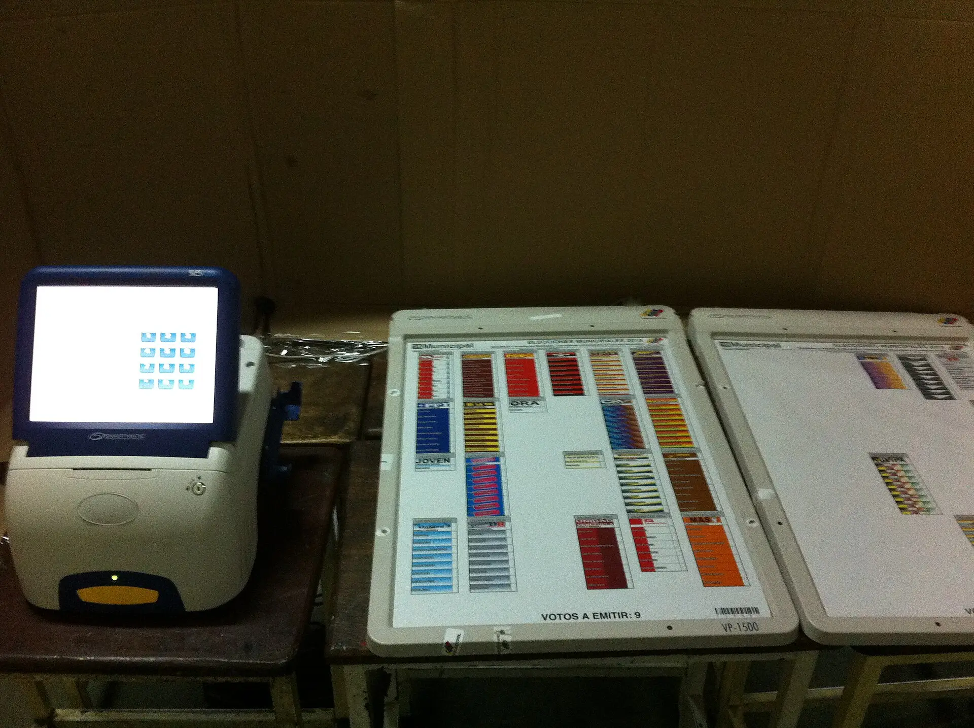 An electronic voting machine and two touch-screen ballot boards sit unattended on tables at a Venezuelan polling station.